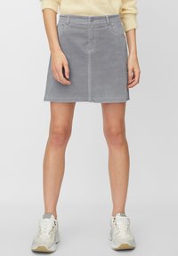 Falda de mezclilla gris con un diseño ajustado, bolsillos delanteros y dobladillo deshilachado. Combinada con zapatillas blancas, presentada sobre un fondo neutro.