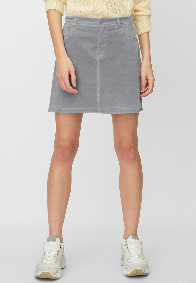 Falda de mezclilla gris con un diseño ajustado, bolsillos delanteros y dobladillo deshilachado. Combinada con zapatillas blancas, presentada sobre un fondo neutro.
