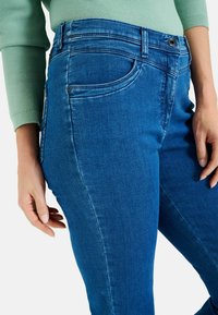 Jeans in denim blu con vita alta, tasche frontali e vestibilità slim. Il tessuto ha una superficie liscia e dettagli di cucitura a contrasto.