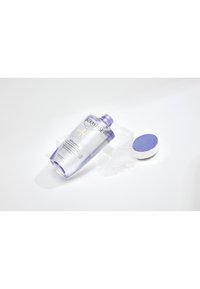 Flacon de soin capillaire Kérastase Blond Absolu avec bouchon violet posé ouvert sur une surface blanche avec un produit clair et gélifié renversé à proximité.