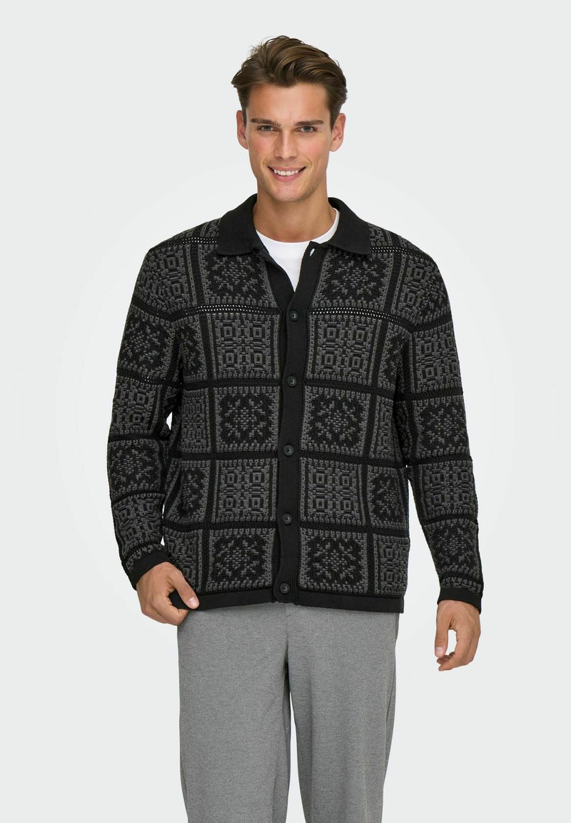 Knappad cardigan med ett geometriskt mönster i svart och grått, tillverkad av strukturerad tyg med krage och ribbad mudd.