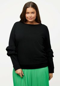 Sweatshirt noir avec des manches volantes, encolure ronde et ourlet côtelé. Associé à une jupe plissée verte, montrant une texture douce.