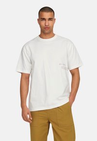 Weißes Baumwoll-T-Shirt mit kurzen Ärmeln, Rundhalsausschnitt und pinkem Drucktext auf der linken Seite. Einfaches, lockeres Design.
