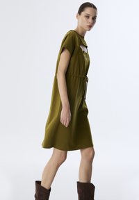Grün knielanges Kleid mit kurzen Ärmeln, Kordelzug taille und einer kleinen Tasche. Hergestellt aus glattem Stoff mit einer lockeren Silhouette.