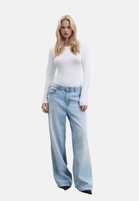 Weißer Langarm-Bodysuit kombiniert mit hellblauen, weit geschnittenen Jeans. Glattes Material, hohe Taille, dezente Ausbleichungen und klassisches Fünf-Taschen-Design.