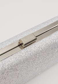 Pochette rectangulaire argentée scintillante avec un fermoir métallique gravé du nom de la marque Mascara.