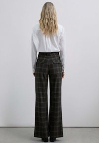 Pantalons à carreaux larges dans des tons sombres, avec une taille haute, des poches arrière et des détails de couture subtile, associés à une chemise blanche à boutons.