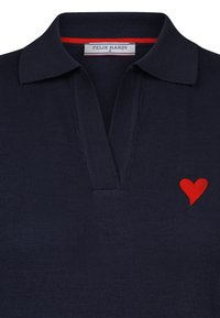 Marinblå polo skjorta med krage, med ett röd broderat hjärta på vänster sida och en röd detalj inuti kragen.