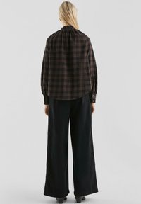 Langsleeve, geruite blouse in donkere tinten met een geplooide halslijn. Gepaard met wijd uitlopende zwarte broek, wat een vloeiende silhouettes creëert.
