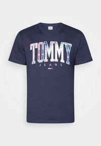 Camiseta de algodón navy con un gran gráfico multicolor de "TOMMY" y acentos de tablero de ajedrez, con el texto "JEANS" debajo. Diseño clásico de cuello redondo.