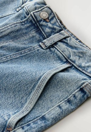 Suurendatud vaade siniste jeanside vöökohta, vöökinnituskohtadele, metalli nupule, millel on tekst "NEXT DENIM", ning detailsele õmblusele.