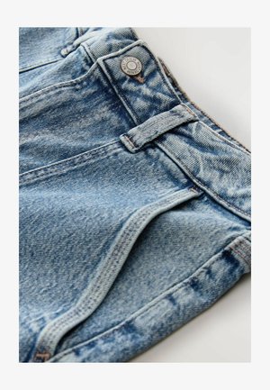 Suurendatud vaade siniste jeanside vöökohta, vöökinnituskohtadele, metalli nupule, millel on tekst "NEXT DENIM", ning detailsele õmblusele.