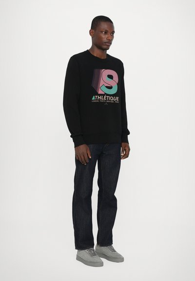 Felpa nera con grafica testuale colorata, indossata con jeans scuri e sneaker grigio chiaro. Tessuto morbido, vestibilità rilassata e polsini a coste.