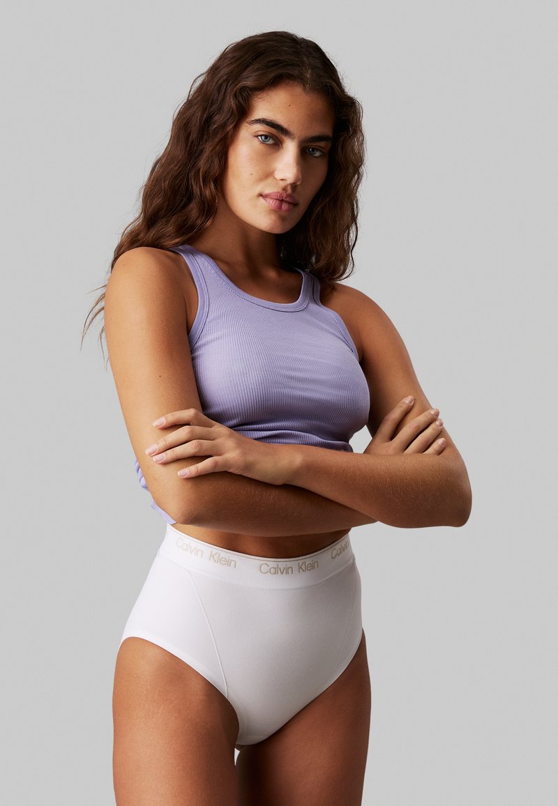 Purple ribbed tank top and white high-waisted underwear with a subtle Calvin Klein logo on the waistband. Smooth fabric, fitted design.