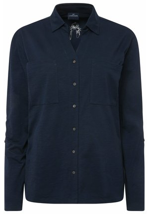 Chemise à manches longues bleu marine en tissu doux et texturé. Elle possède un col en V, deux poches sur la poitrine et une rangée de boutons sur le devant.
