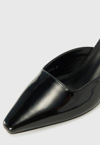 Chaussure femme noire brillante à bout pointu, talon bas et finition en cuir lisse sur un fond clair uni.