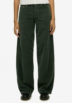 Groene corduroy broek met wijde pijpen en ribbelstructuur, met voorzakken en een hoge taille. Zwarte schoenen zichtbaar aan de onderkant.