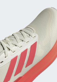 Jasne sneakersy z teksturowaną górą, z białymi sznurówkami, czerwonymi akcentami po bokach oraz gumową podeszwą oznaczoną "CLOUDFOAM".