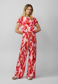 Jumpsuit a maniche corte con motivo rosso e rosa, dalla vestibilità comoda. Presenta pantaloni plissettati e una cintura elastica. Tessuto morbido e leggero.