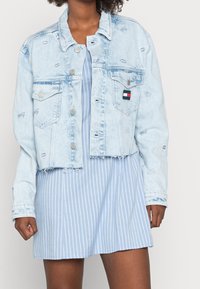 Ljusblå denimjacka med kortad design, fransad nederkant och två bröstfickor. Har subtil slitning och ett litet logobadge.