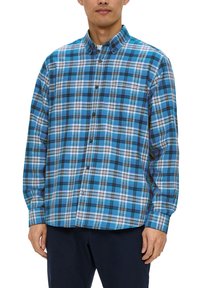 Chemise à carreaux bleue à boutons, présentant un mélange de bleu clair et foncé, de blanc et de noir, avec un col et des manches longues.
