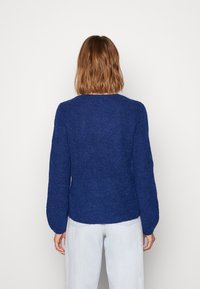 Sweter dzianinowy w głębokim niebieskim kolorze, z okrągłym dekoltem i długimi rękawami. Teksturowany materiał w luźnym kroju, idealnie pasuje do jasnych dżinsów.