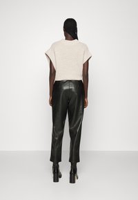 Kortärmad, beige stickad tröja parat med svarta läderbyxor, med slim fit och synliga sömdetaljer. Svarta ankelstövlar fulländar looken.