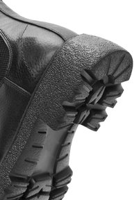 Ingrandimento di una scarpa in pelle nera che mostra il suola in gomma testurizzata dettagliata con profondi motivi di battistrada per grip e durata.
