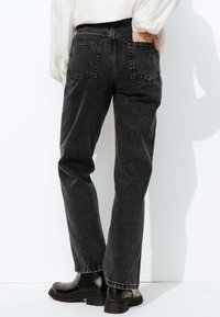 Jeans en denim noir à coupe droite, dotés de deux poches arrière, de détails cousus et d'une texture usée. Associés à des bottines noires.