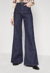 Wide-leg denim pants in dark blue, featuring a high waist, belt loops, and contrasting stitching. Smooth texture with a subtle sheen.
