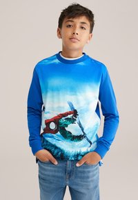 Mėlynos ilgomis rankovėmis sporto marškiniai su snieglentininko veiksmo grafika. Medžiaga yra minkšta, su gradientiniu mėlyno ir balto fono deriniu ir spalvingais akcentais.