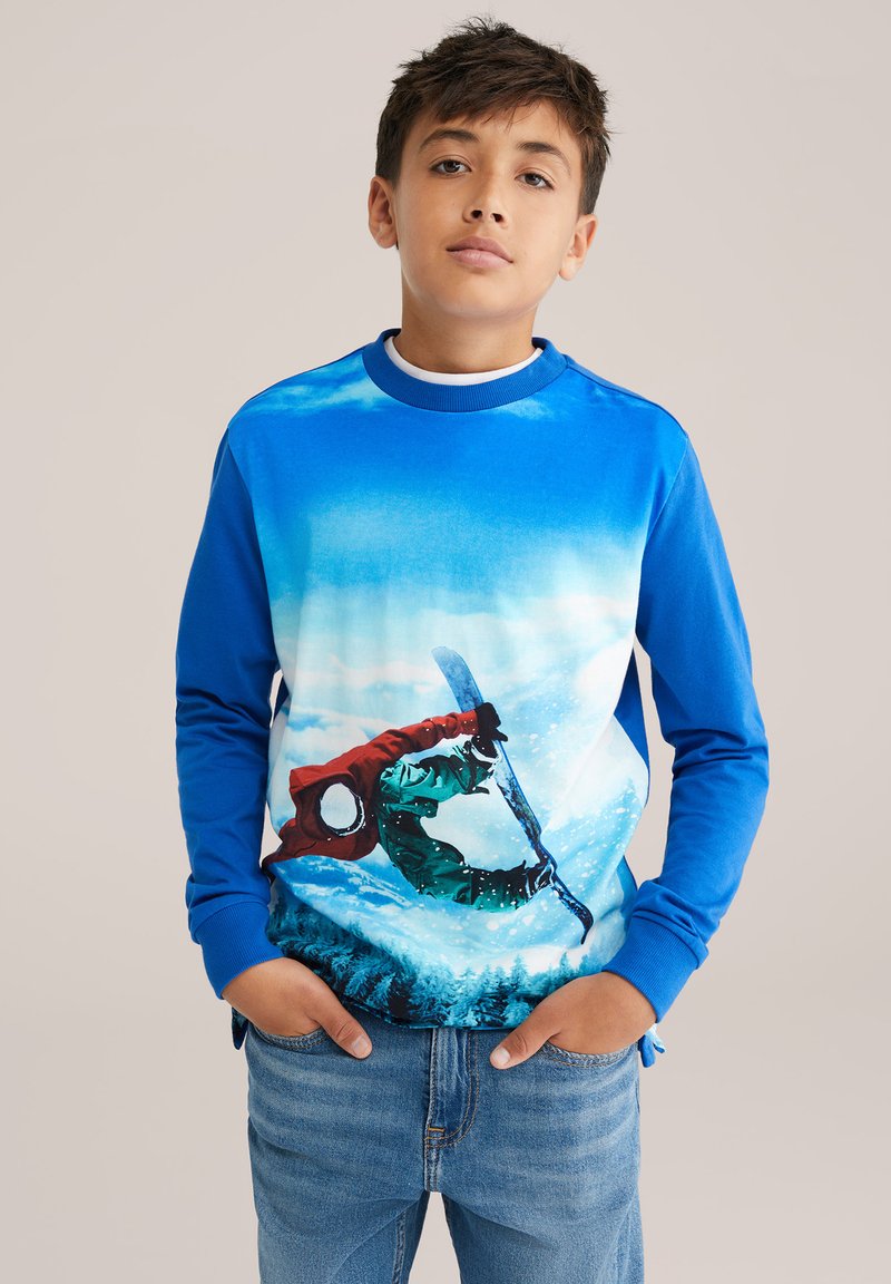 Mėlynos ilgomis rankovėmis sporto marškiniai su snieglentininko veiksmo grafika. Medžiaga yra minkšta, su gradientiniu mėlyno ir balto fono deriniu ir spalvingais akcentais.