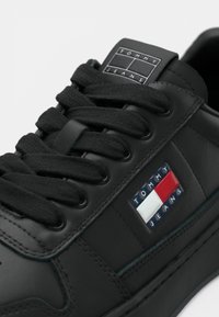 Baskets en cuir noir avec lacets noirs, avec un patch logo Tommy Jeans en rouge, blanc et bleu sur le côté et la languette.
