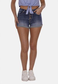 Shorts in denim con risvolti, di un colore lavato medio, con chiusura a cinque bottoni e tasche frontali. Abbinati a sneakers bianche.