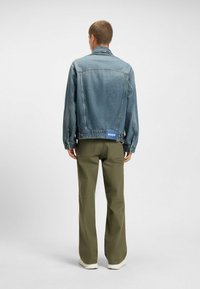 Jeansjacka i ljusblått med rak skärning, synlig sömnad och en varumärkespatch. Matchas med olivgröna byxor och sneakers.