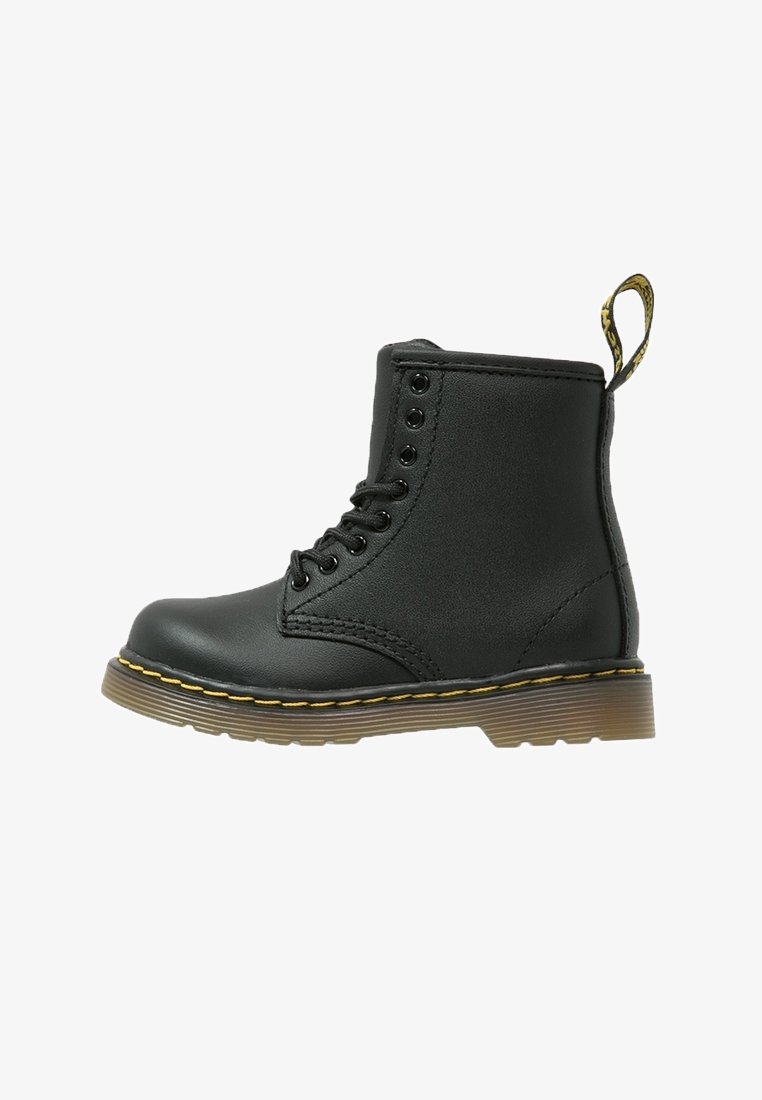 Bottine en cuir noir à la cheville avec huit œillets, couture jaune sur la semelle, et une languette en boucle pour un enfilage facile sur fond blanc.