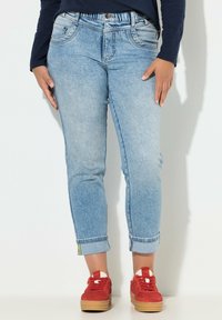 Jeans di denim azzurro chiaro con design aderente, risvoltini, cinque tasche e vita elasticizzata. Abbinati a sneakers in camoscio rosso.