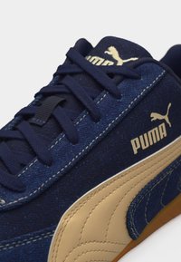 Navy blue sneaker with beige Puma stripe and logo, dark blue laces, and detailed stitching on a white background.