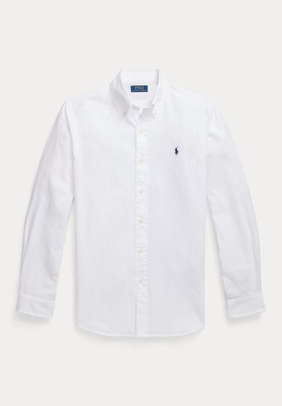 Λευκό πουκάμισο με μακριά μανίκια και κουμπιά, με μυτερό γιακά, που διαθέτει μικρό ναυτικό λογότυπο στο αριστερό στήθος και κίτρινα κουμπιά. Λείο ύφασμα.