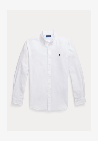 Λευκό πουκάμισο με μακριά μανίκια και κουμπιά, με μυτερό γιακά, που διαθέτει μικρό ναυτικό λογότυπο στο αριστερό στήθος και κίτρινα κουμπιά. Λείο ύφασμα.