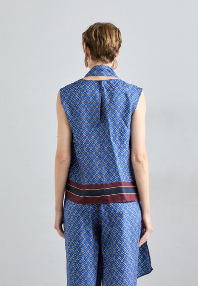 Ärmelloses Oberteil mit blauem Muster, hohem Kragen, Rückenfalte und einem burgunderfarbenen horizontalen Akzentband am Saum. Glatte Stofftextur.