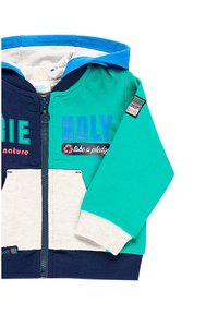 Children's zip-up hoodie in blue, green, and navy. Cotton blend, features front pockets, graphic text, and striped branding on the sleeve.