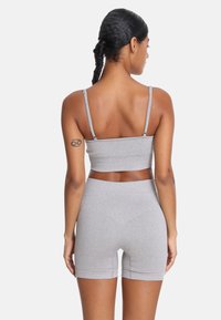 Sivi športni komplet, ki vsebuje prilegajoč se crop top in kratke hlače z visokim pasom, izdelan iz raztegljive tkanine. Izstopajo tanke naramnice in gladka tekstura.