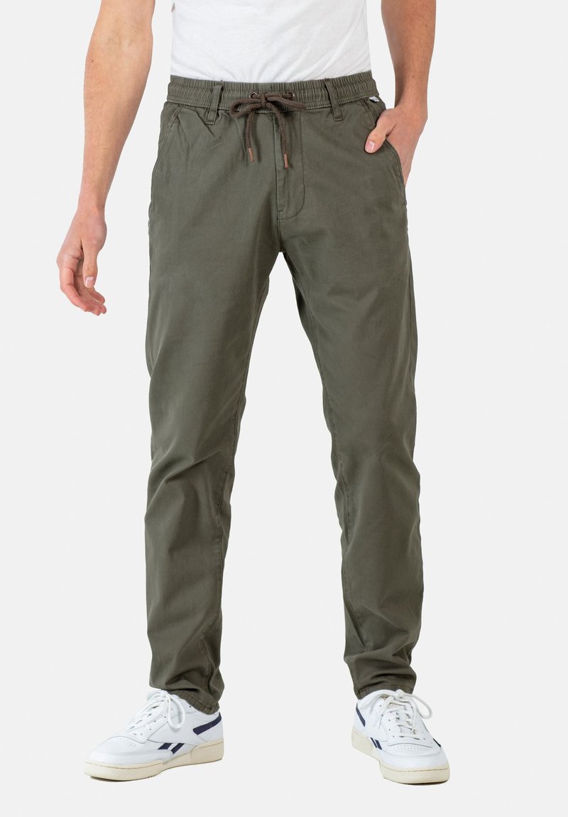 Pantalones de tiro elástico verde oliva en tejido ligero; cuenta con bolsillos frontales y una cinturilla elástica; combinados con zapatillas blancas.