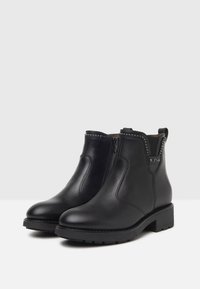 Stivali ankle in pelle nera con zip laterale, caratterizzati da una suola testurizzata e dettagli decorativi in rivetti alla caviglia. Design con tacco a blocco.