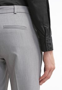 Pantalones grises a medida con una textura suave, que cuentan con un bolsillo trasero y una camisa negra elegante con puños abotonados.