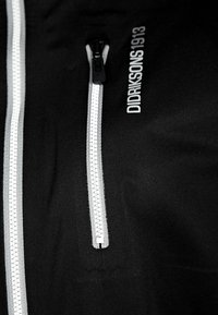 Svart jacka med en framträdande dragkedja med ett silverhandtag, och "DIDRIKSONS 1913" tryckt i vitt på tyget.