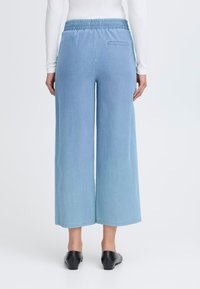 Ljusblå vida byxor med elastisk midja, med en enda bakficka och en slät denimtextur. Matchas med svarta skor.