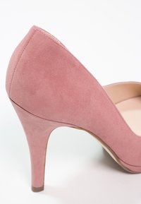 Chaussure à talon haut en suede rose avec une structure effilée et une texture lisse. Présente un talon fin et un design à bout rond.