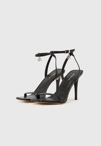 Μαύρα σανδάλια με ψηλό τακούνι και λεπτά λουράκια, με υφή λείας δέρματος, σχέδιο ανοιχτής μύτης και μικρό διακοσμητικό κρεμαστό στο λουρί του αστραγάλου.